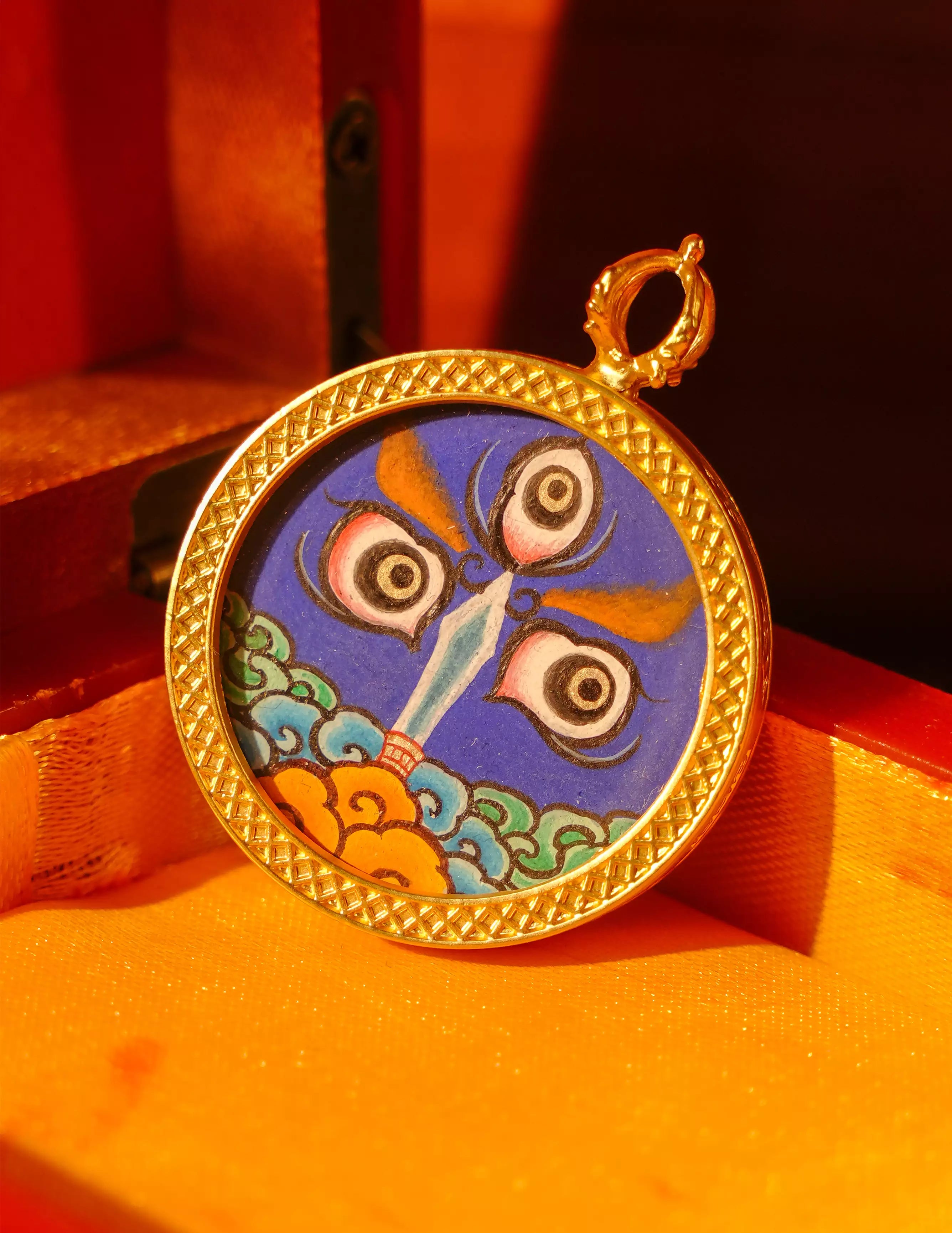 Sharp close-up of an Acalanatha miniature pendant, with a richly detailed gold-toned frame and blue painted composition